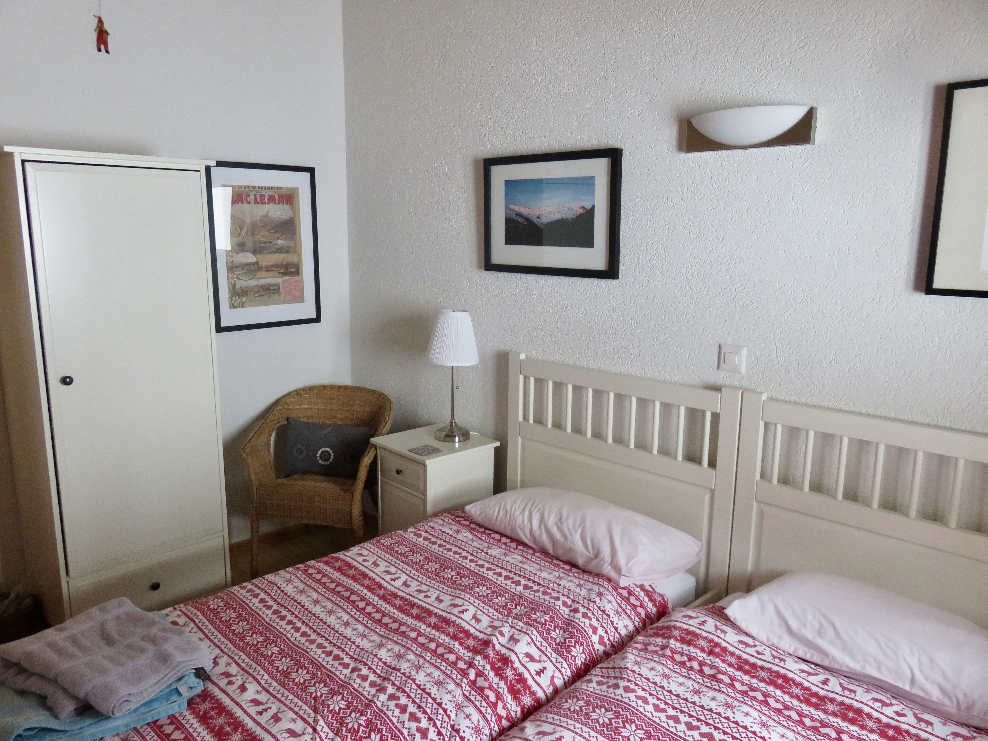 A bedroom with a bed, a nightstand, a chair, a wardrobe, and two framed pictures on the wall.