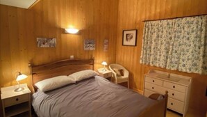 Ein Schlafzimmer mit Holzwandverkleidung, einem Bett, Nachttischen, einem Sessel und einer Kommode.
