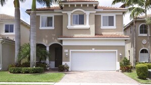 A two-story house with a garage, palm trees, and a well-maintained lawn.