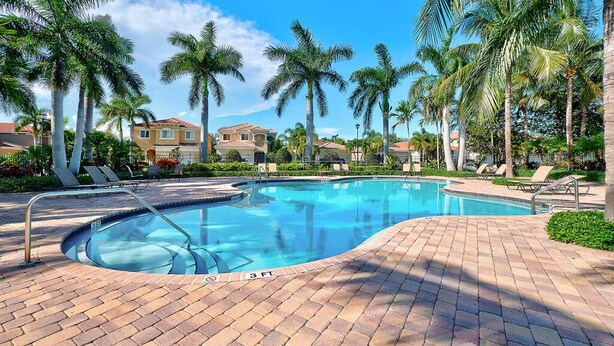 A swimming pool with a brick deck, surrounded by palm trees and lounge chairs.