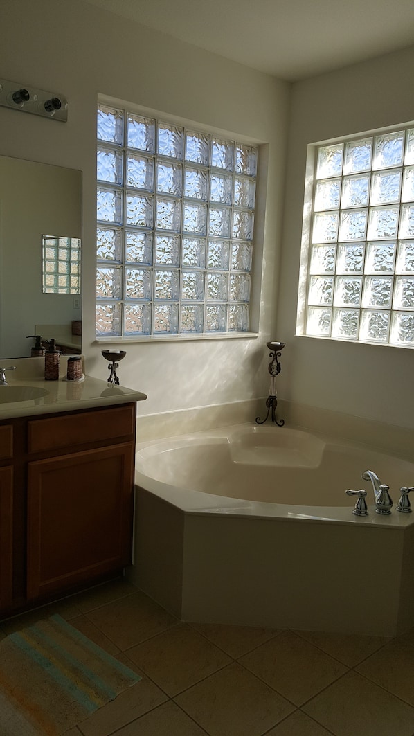 Une salle de bain avec une baignoire sur pieds, un meuble-lavabo avec un miroir et deux fenêtres ornées de vitraux décoratifs.