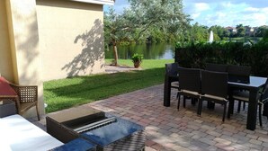 An outdoor patio with a table and chairs, a small garden, and a view of a lake and buildings in the background.