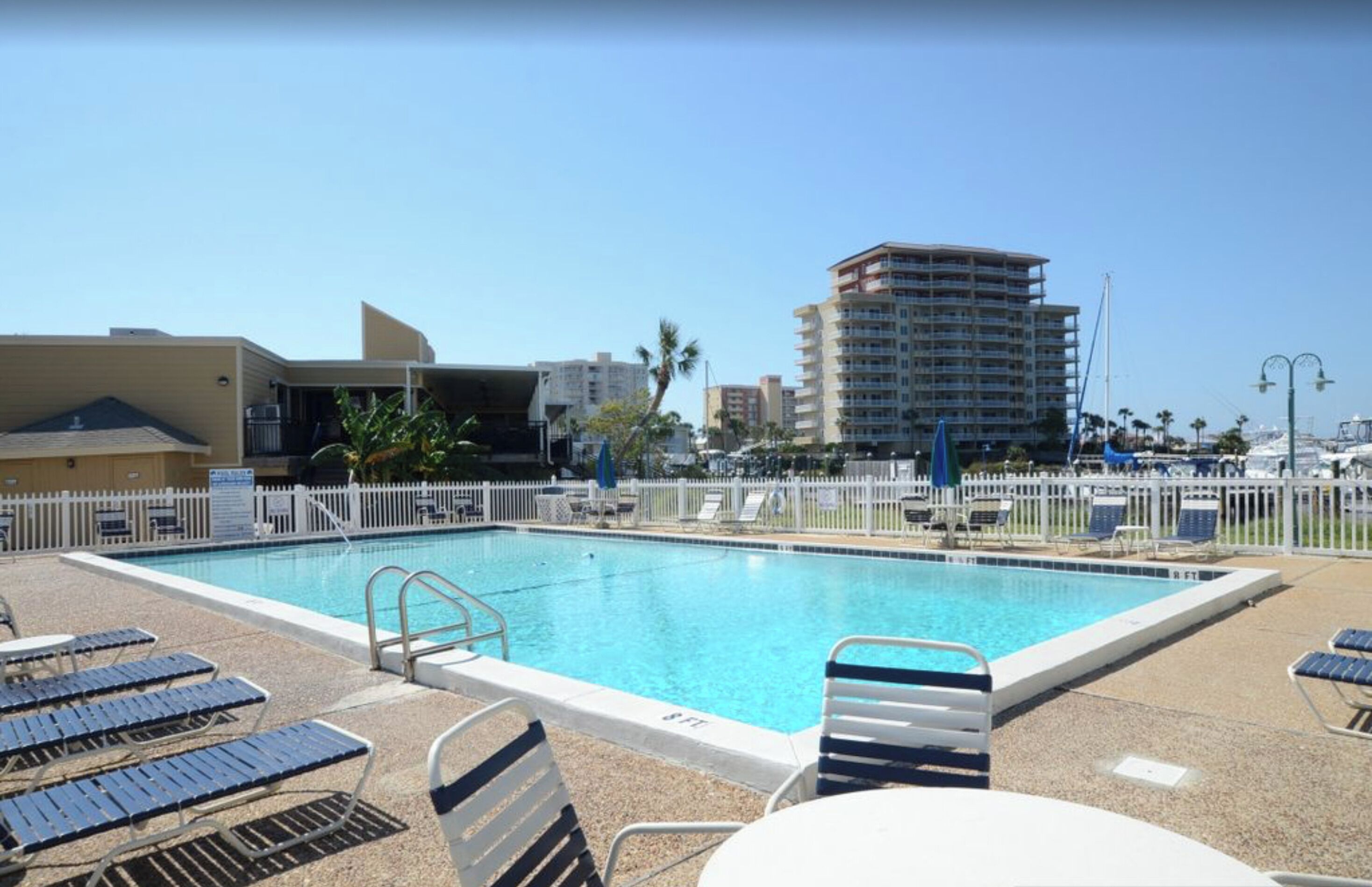A swimming pool with lounge chairs and a white fence.