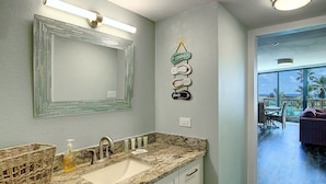 A bathroom with a granite countertop, a mirror, and a wall decoration. - Escape to Mayan Princess 213 Beachfront Getaway! (Port Aransas)