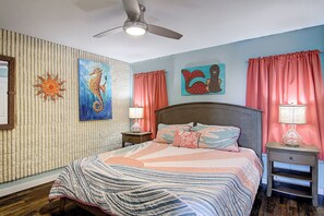 A bedroom with a bed, a nightstand, a ceiling fan, and artwork on the walls. - Escape to Mayan Princess 213 Beachfront Getaway! (Port Aransas)
