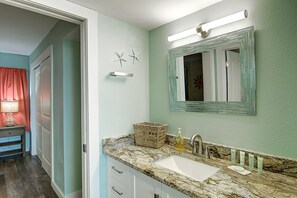 A bathroom with a marble sink, a mirror with a decorative frame, and a wicker basket on the countertop. - Escape to Mayan Princess 213 Beachfront Getaway! (Port Aransas)