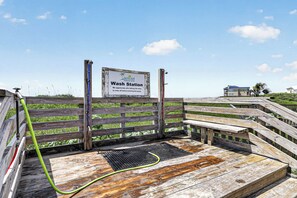 A wooden wash station with a sign, a hose, and a metal grate.