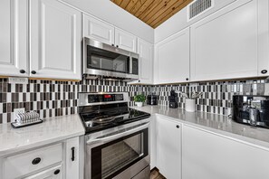 A modern kitchen with white cabinetry, a built-in oven, a microwave, and a coffee maker.