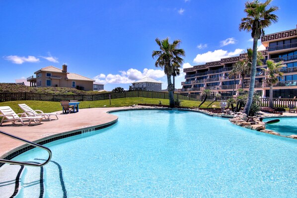 A swimming pool with lounge chairs and a no diving sign, surrounded by buildings and palm trees.