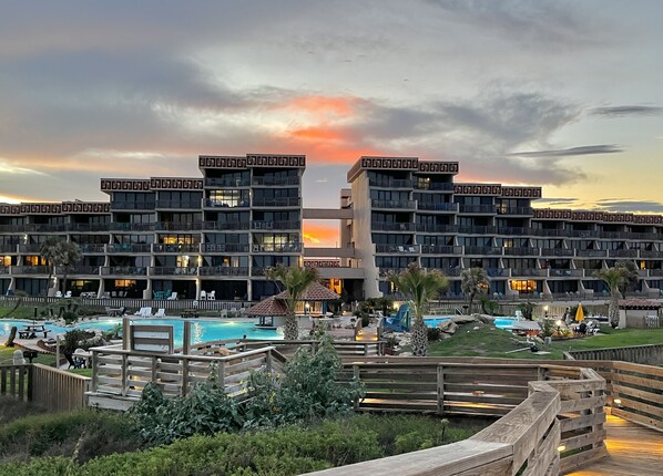 A hotel with multiple balconies, a swimming pool, and a sunset view.
