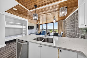 A modern kitchen with a built-in dishwasher, a large window offering a view, and a wooden ceiling.