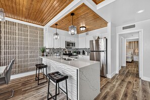 A modern kitchen with a central island, bar stools, and a wooden ceiling.
