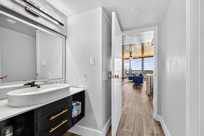 A modern bathroom with a large mirror, white walls, and a wooden floor.