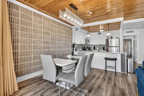 A modern kitchen with a central island, grey upholstered chairs, and a wooden ceiling.