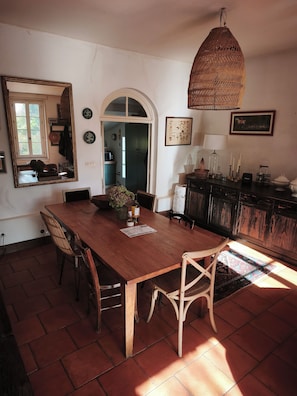 Un coin repas avec une table en bois, des chaises, un luminaire suspendu et une vue sur la cuisine.