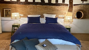 Un dormitorio con una cama grande, dos mesitas de noche con lámparas, techo de madera y pared de piedra.