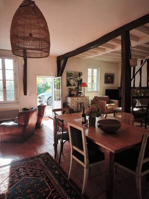 Un coin repas avec une table en bois, des chaises, un luminaire suspendu en fibres tressées et une vue sur l’extérieur.