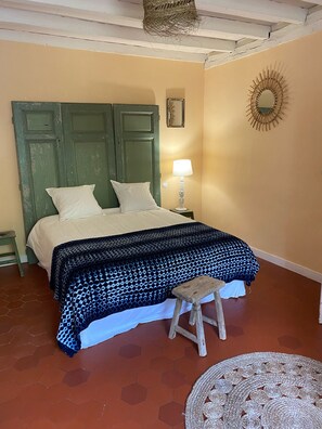A bedroom with a green door, a bed with white and blue patterned bedding, a small stool, a nightstand with a lamp, and a decorative mirror on the wall. - Charming 17th century house on 1 ha of land 4 minutes from Bergerac (Bergerac)