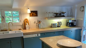 Una cocina con armarios azules, un fregadero, un lavavajillas Bosch, una cafetera y un colgante de luz.