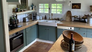 Una cocina con armarios azul verdosos, una encimera de madera, un lavabo y una botella de vino sobre la encimera.