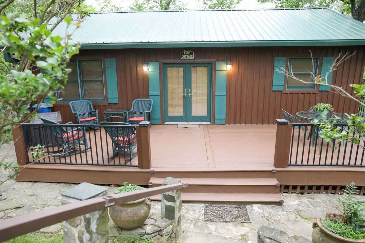 A wooden cottage with a porch, two chairs, a table, and a sign reading 'Fern Cottage.'