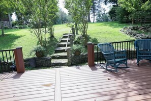 Une terrasse en bois avec un escalier en pierre menant à une cour gazonnée.