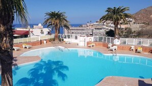 A swimming pool with a view of a coastal town, palm trees, and a supermarket sign. - Casa La Moringa - Holiday house close to the beach (Los Caideros)