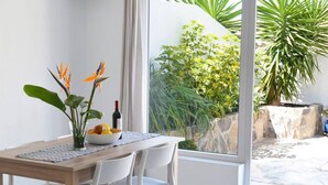 A dining area with a wooden table, white chairs, a vase with flowers, a bowl of fruit, and a bottle of wine. - Casa La Moringa - Holiday house close to the beach (Los Caideros)