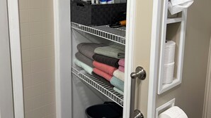 A bathroom with a toilet paper holder, a black bucket, and a shelf with towels and cleaning supplies. - Quiet home on horse farm, halfway between Paducah & Wickliffe. Close to 60 & 286 (Kevil)