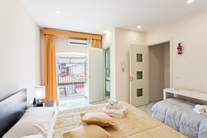A hotel room with a bed, a bedside table, a nightstand, a window with curtains, a door, and a view of the outside.