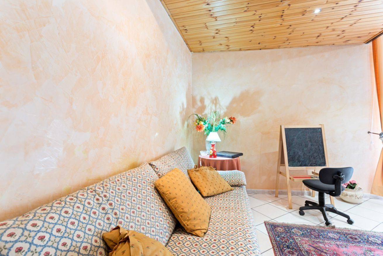 A cozy room with a patterned sofa, a small table with a lamp, a black office chair, and a chalkboard on a stand.