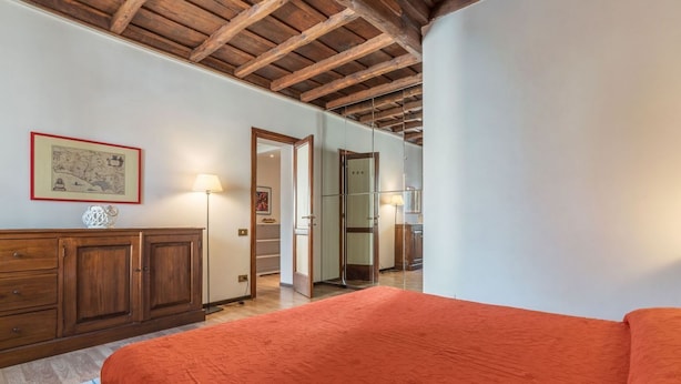 Un dormitorio con techo de madera, una cama con colcha naranja, un aparador de madera y un espejo.