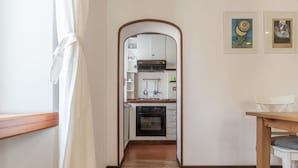 Un pasillo estrecho que conduce a una cocina con armarios blancos, un horno negro y una mesa de madera.