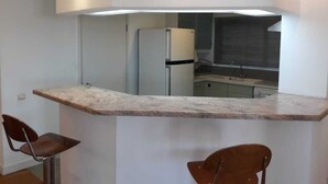 Una cucina moderna con un piano di lavoro in marmo, due sgabelli da bar, un frigorifero e una finestra con persiane.