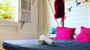 Een bed met een blauwe matras, witte en roze kussens en een opgerolde witte handdoek.