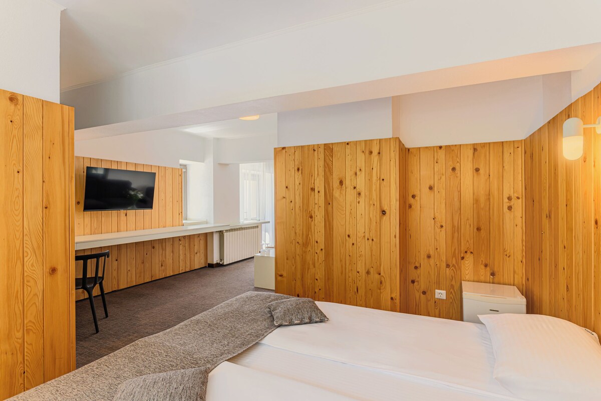 A hotel room with a bed, a desk, a chair, and a television.