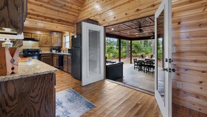 Ein modernes Blockhaus mit einer Küche, die sich durch Granitarbeitsplatten, einen Kühlschrank und Holzschränke auszeichnet. Ein Glastür öffnet sich zu einer Außenpatio mit Whirlpool und Sitzgelegenheit.