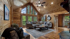 Ein gemütliches Blockhaus-Interieur mit einem Ecksofa, einem Couchtisch und einer großen Uhr an der Wand.