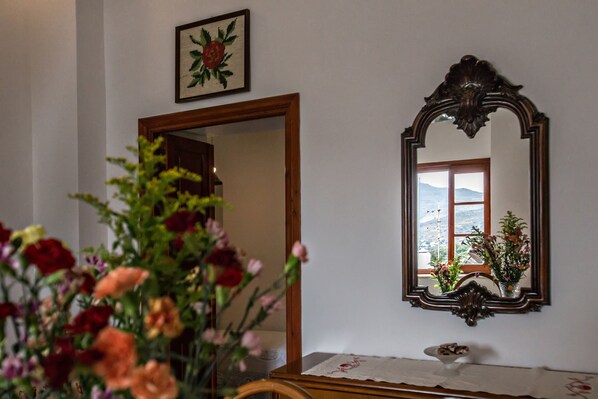 A room with a wooden door, a mirror with an ornate frame, and a floral arrangement on a table.