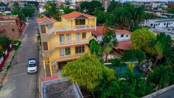 Un edificio amarillo de varios pisos con balcones, rodeado de exuberante vegetación y otras edificaciones residenciales.