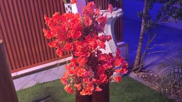 Una planta en maceta con flores rojas en un jardín con césped artificial.