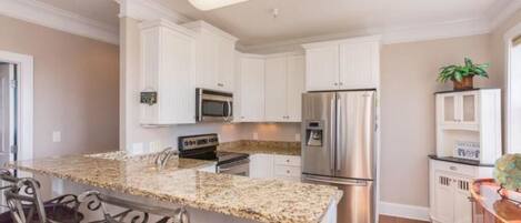 A kitchen with white cabinets, stainless steel appliances, granite countertops, and a bar area with purple chairs.