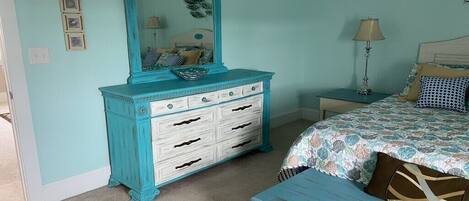A bedroom with a turquoise dresser, a bed with patterned bedding, and a bedside table with a lamp.