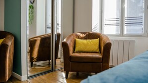 A room with a brown leather armchair with a yellow pillow, a glass door, and a window with blinds. - BnB Epernay   Studio 86   Your Cozy Nest for Two in Épernay (Épernay)