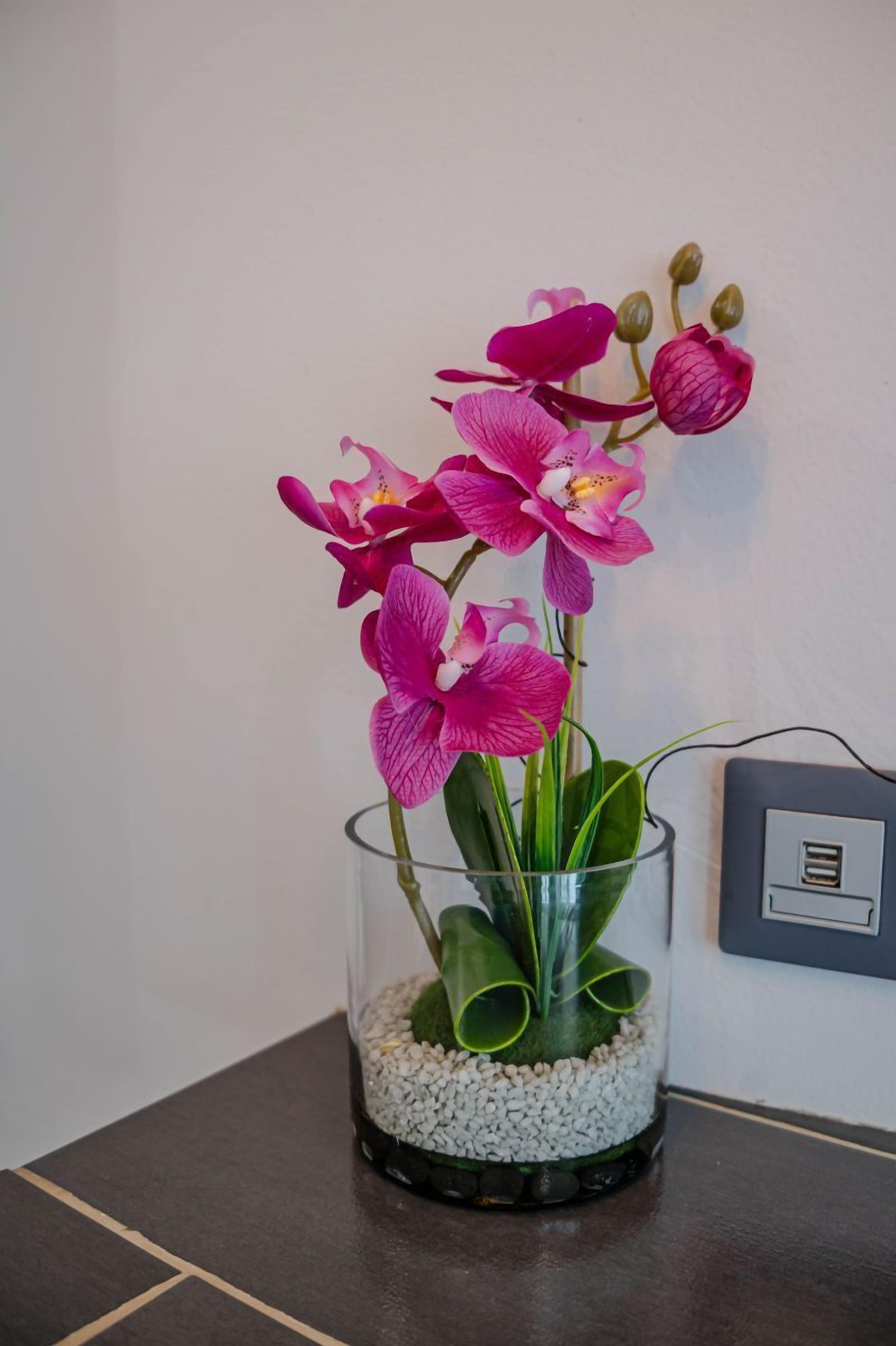 A glass vase with pink orchids on a dark tiled surface.