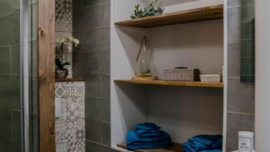 A modern bathroom with a toilet, a shower, and a sink. There are shelves with decorative items and folded towels. - BnB Epernay   Studio 86   Your Cozy Nest for Two in Épernay (Épernay)