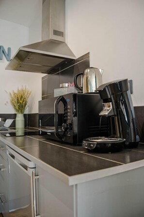 Une cuisine moderne équipée d’une machine à café, d’une bouilloire et d’une hotte aspirante en acier inoxydable.