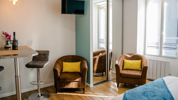 A modern room with a TV mounted on the wall, two leather armchairs with yellow cushions, a wooden floor, and a window providing natural light. - BnB Epernay   Studio 86   Your Cozy Nest for Two in Épernay (Épernay)