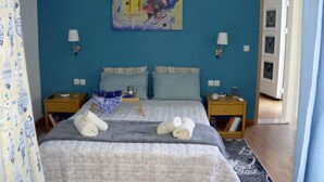 A bedroom with a large bed, two bedside tables, a nightstand, a painting on the wall, and a door leading to another room.