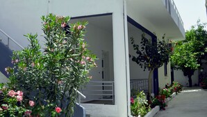 A white building with a balcony, potted plants, and a staircase leading to an entrance.